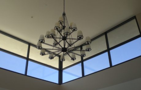 A chandelier in the center of a room with two windows.