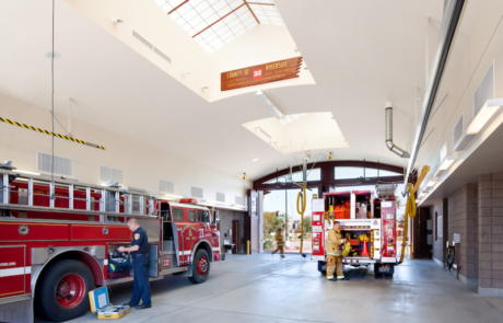 A fire station with two firemen standing next to the trucks.